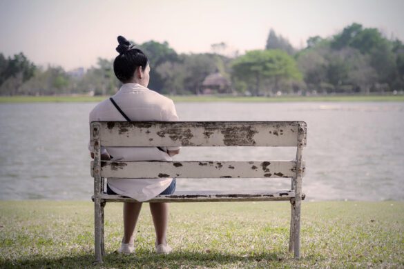 A woman sitting by a lake reflecting on the loss of a loved one. She is grieving the loss deeply. Our therapists at the Relationship & Intimacy Center can help you grieve your loss in a healthy way.